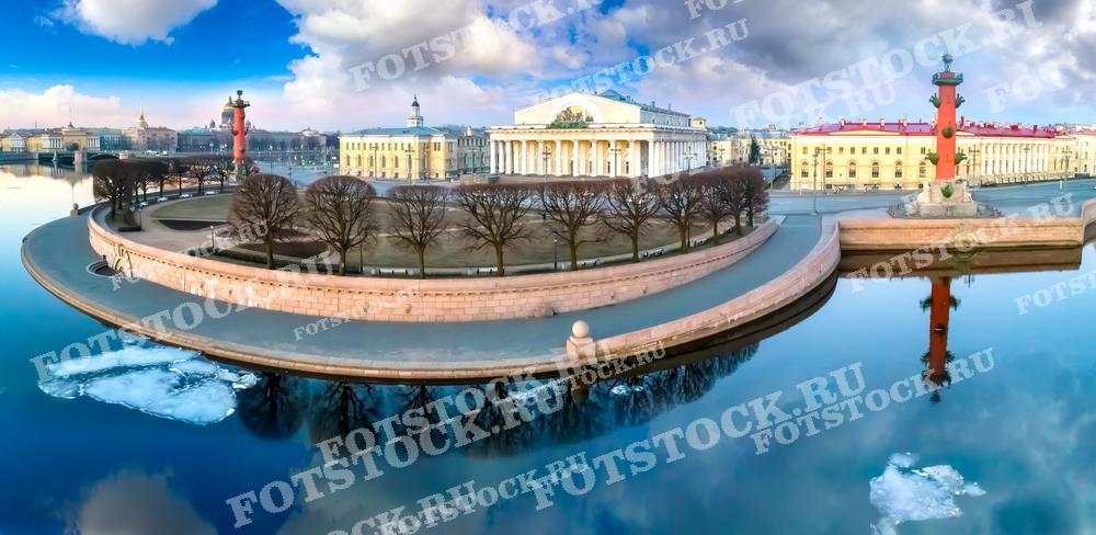 Эта фотография демонстрирует Стрелку Васильевского острова в Санкт-Петербурге. Съемка произведена с воздуха, и отчётливо видно отражение объектов в воде, придающее композиции зеркальную симметрию. Небо безоблачное с лёгкими разводами облаков. Изображение может быть использовано для туристических проспектов, учебных материалов по истории архитектуры, а также как рекламный постер или в качестве фотообоев для интерьера.